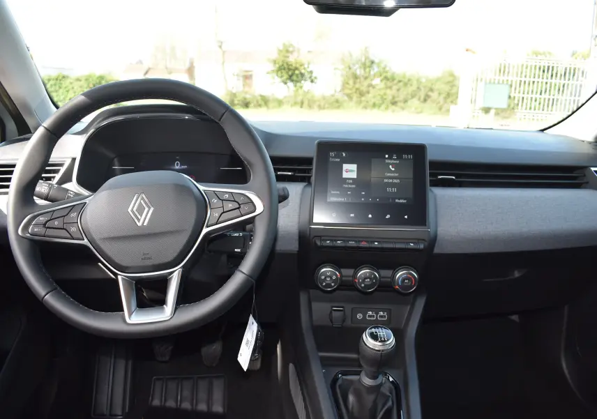 Intérieur de la Renault Clio V TCE 90 gris, vue de face sur le volant, tableau de bord et levier de vitesse manuel.