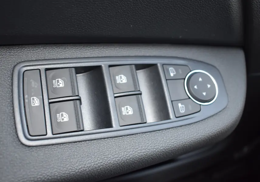 Gros plan sur les commandes de lève-vitres et réglage des rétroviseurs côté conducteur d'une Renault Clio V gris 2024.