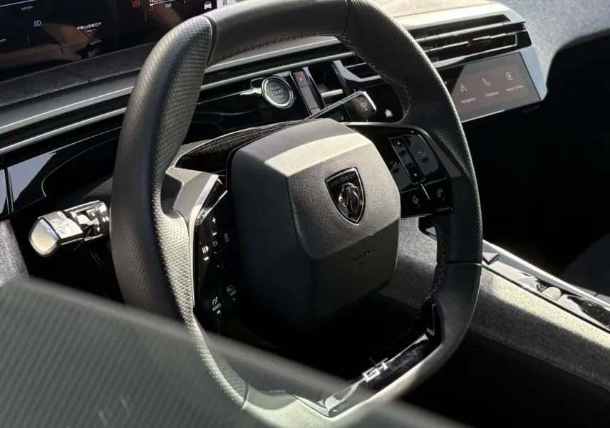 Gros plan sur le volant compact noir perforé avec badge GT du Peugeot 3008 Hybrid 2025, intérieur Alcantara gris.