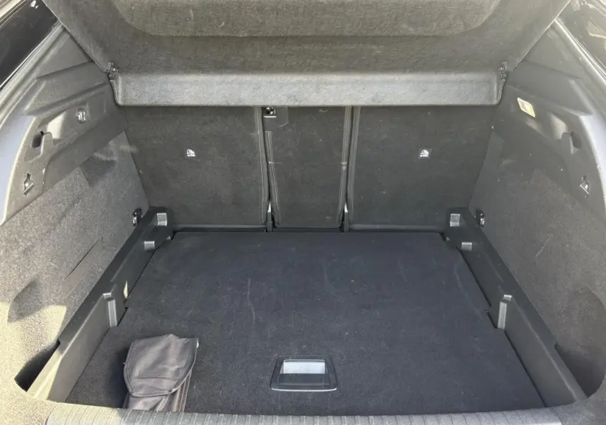 Coffre ouvert vu de l'arrière du Peugeot 3008 Hybrid 145 GT, intérieur noir avec tapis de sol et rangement intégré.