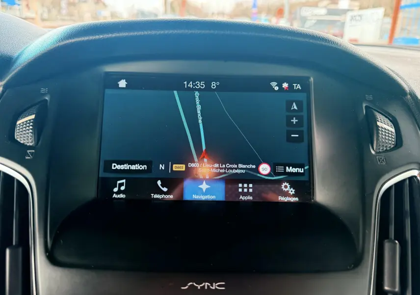 Vue intérieure du poste de conduite de la Ford Focus 1.5 TDCI gris, avec volant multifonction et écran tactile central allumé.