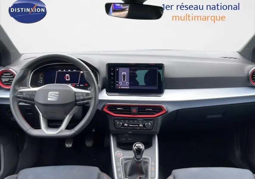 Vue intérieure frontale du tableau de bord du SEAT Arona 2025 avec volant multifonction et touches rouges autour des aérateurs.