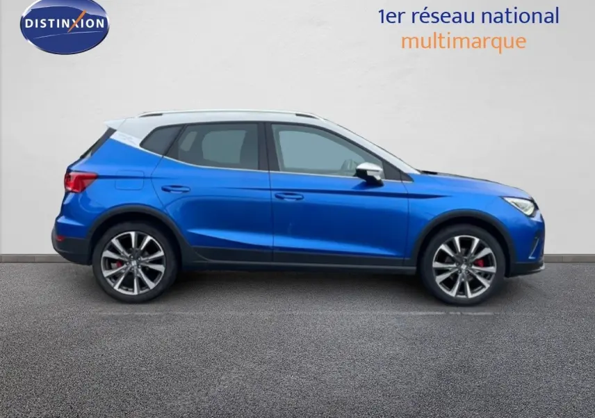 Vue de profil côté gauche d'un SEAT Arona bleu saphir avec toit blanc, jantes alliage et étriers rouges visibles.
