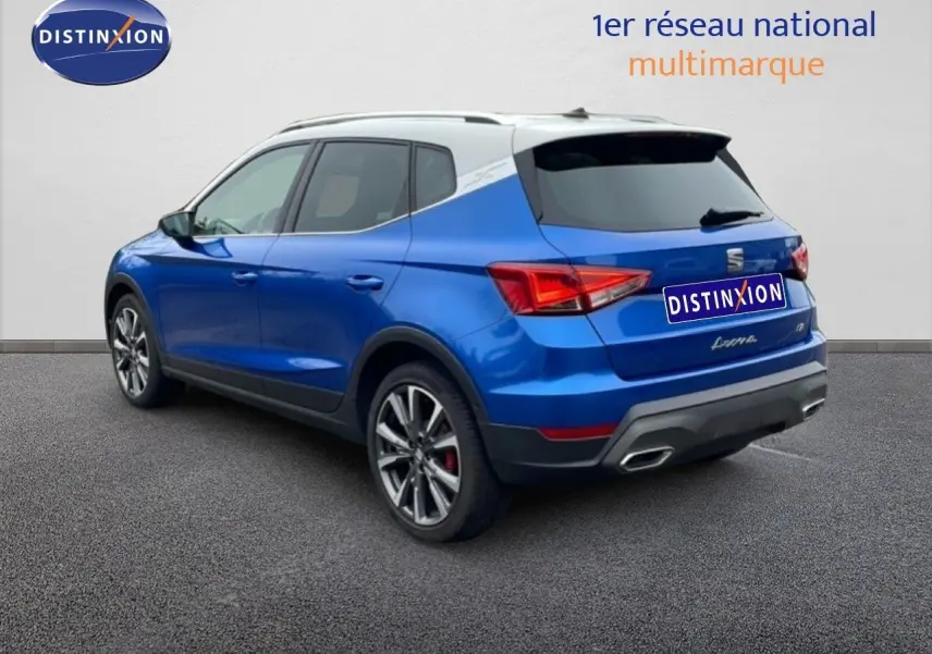 Vue 3/4 arrière d’un SEAT Arona bleu saphir métal avec toit blanc et jantes alliage, sur fond neutre.