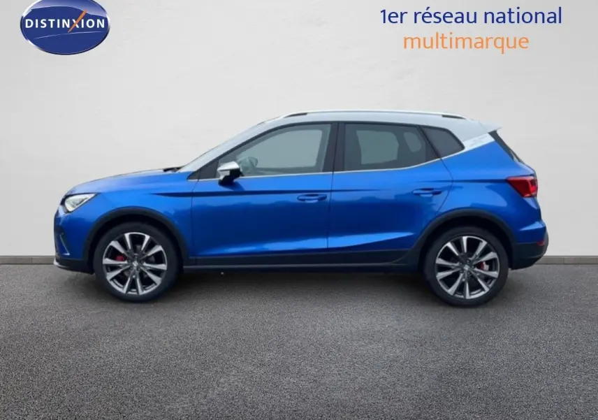 Profil côté gauche d'un SEAT Arona 2025 bleu saphir avec toit blanc, jantes alliage et détails sportifs rouges.