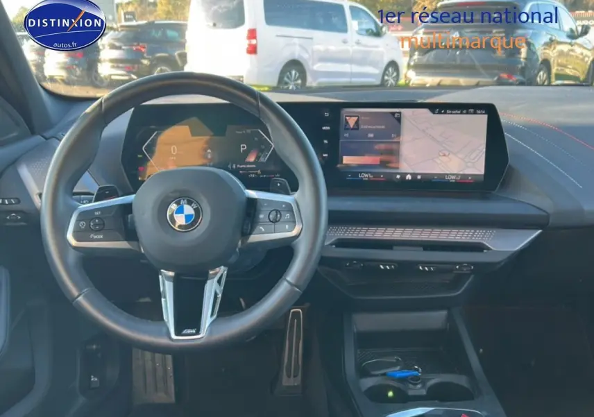Vue intérieure avant du tableau de bord et volant BMW Série 1 blanc alpin, avec écran tactile et commandes au volant.