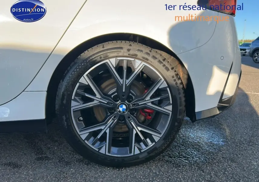 Gros plan sur la roue arrière droite d'une BMW Série 1 blanche avec jante 18 pouces bicolore et étrier de frein rouge.