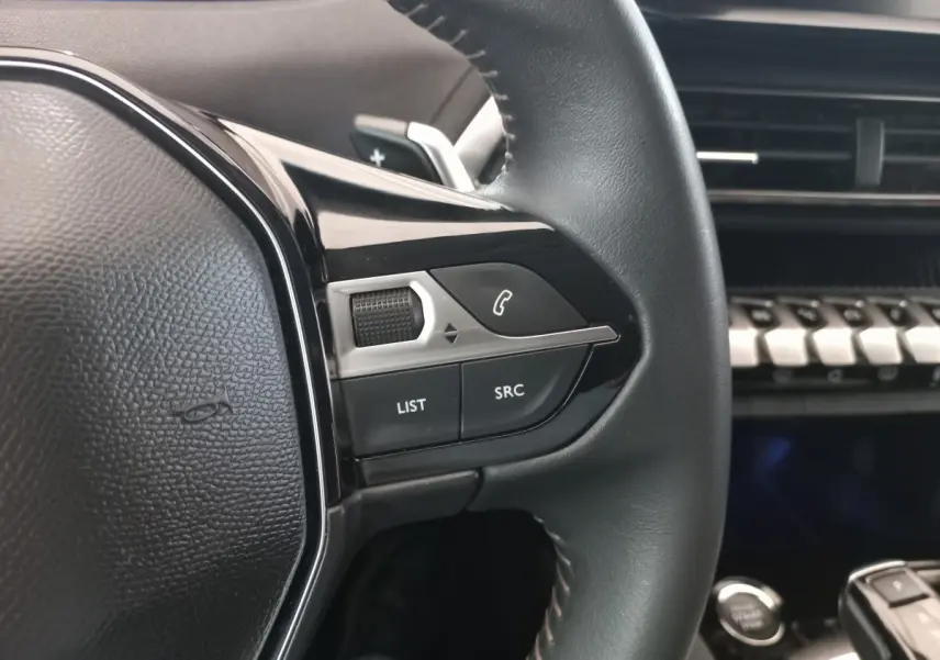 Gros plan sur les commandes au volant cuir noir du Peugeot 3008 2022, avec tableau de bord et touches piano visibles en arrière-plan.