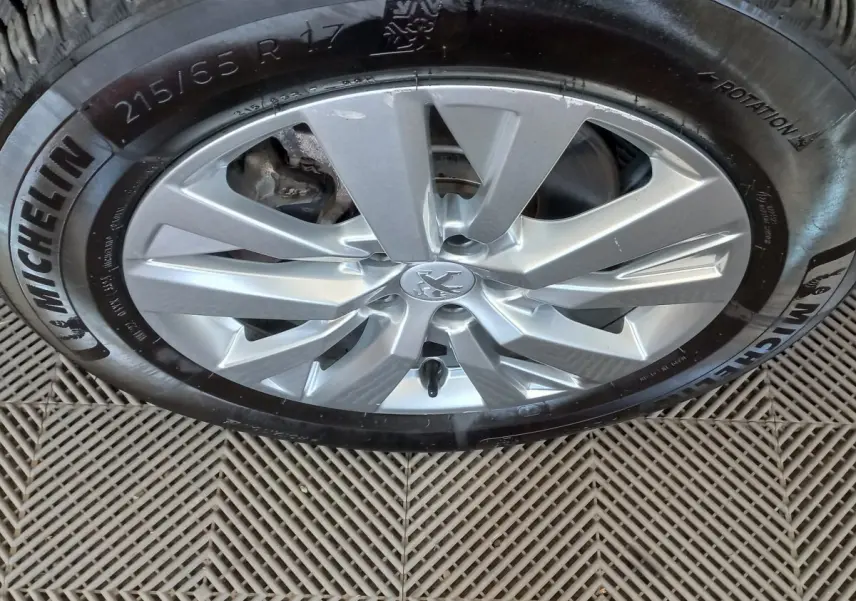Gros plan sur la roue avant droite du Peugeot 3008 noir, jante alliage argentée avec logo Peugeot central.