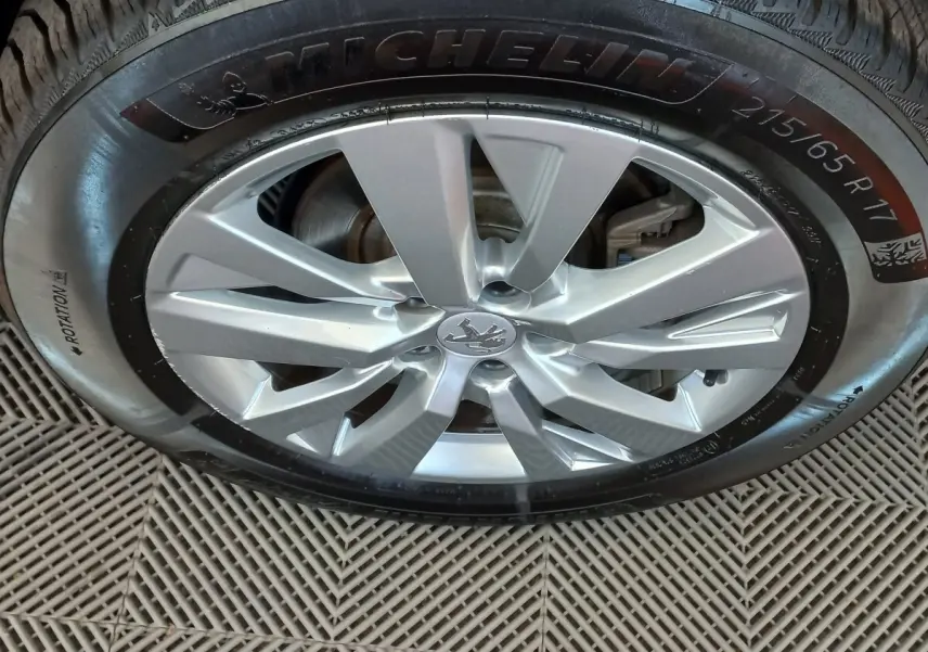 Gros plan sur la jante alliage argentée avec logo Peugeot, montée sur pneu Michelin 215/65 R17.