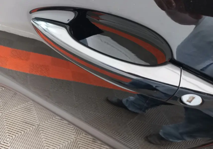 Poignée de porte côté droit noire brillante du Peugeot 3008 PureTech 130, reflet du sol et d'une personne visible.