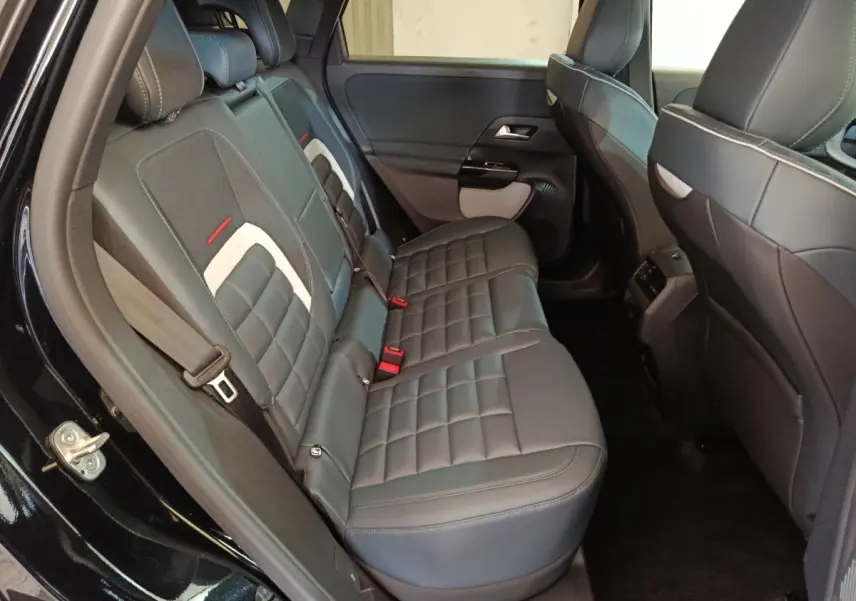Vue intérieure côté gauche des sièges arrière noirs en cuir du Citroën C5 Hybride 2026 avec surpiqûres blanches et ceintures rouges.