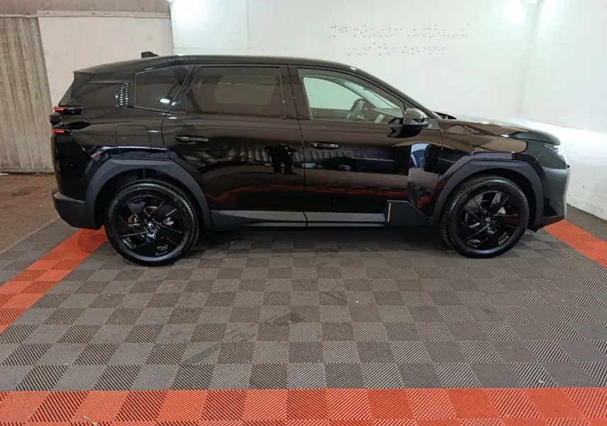 Vue de profil côté gauche d'une Citroën C5 Hybride noire avec jantes noires dans un garage éclairé.