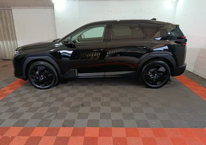 Profil côté gauche d'un SUV Citroën C5 hybride noir avec jantes noires, dans un garage au sol gris et rouge.