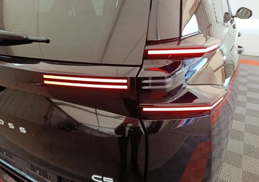 Feu arrière droit allumé d'une Citroën C5 noire, vue rapprochée du coin arrière avec reflets sur la carrosserie.