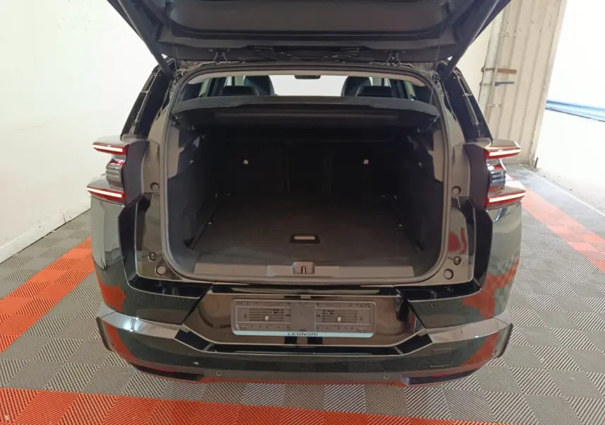 Coffre ouvert d'une Citroën C5 Hybride noire vue de l'arrière, avec feux arrière LED distinctifs allumés.