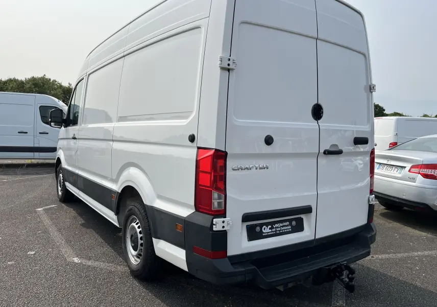 Vue 3/4 arrière droite d'un Volkswagen Crafter blanc fourgon avec hayon et attelage de remorque visible.