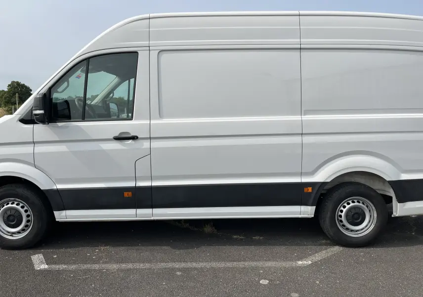 Profil côté gauche d'un fourgon Volkswagen Crafter blanc 2019 avec bande noire et jantes acier simples.