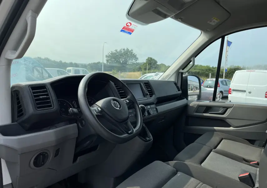 Intérieur côté conducteur du Volkswagen Crafter blanc 2019, tableau de bord et sièges en tissu gris visibles de profil droit.