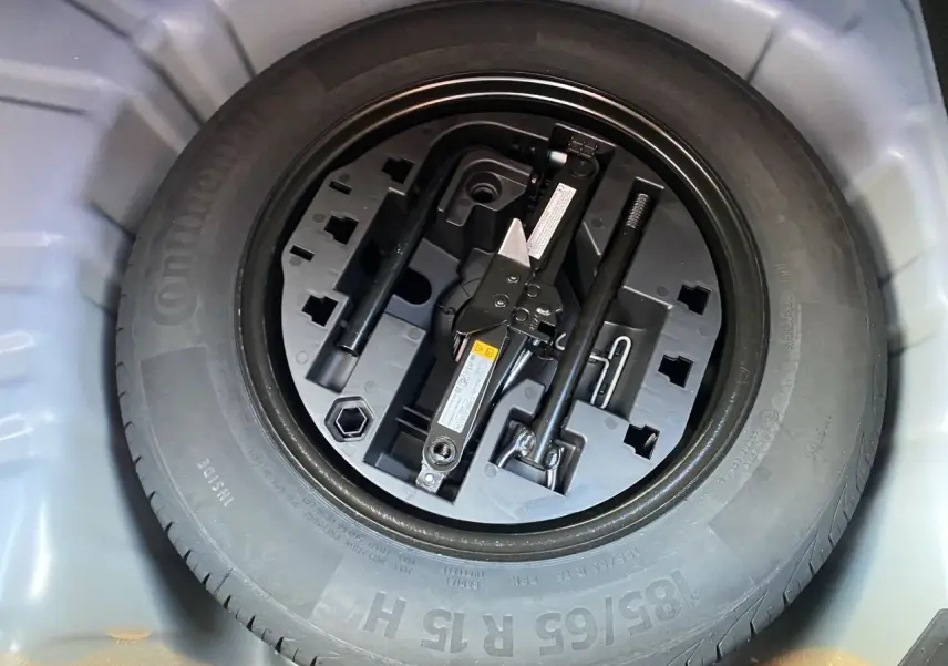 Vue en plongée sur la roue de secours et le cric dans le coffre d'une Renault Clio V bleu Iron 2025.