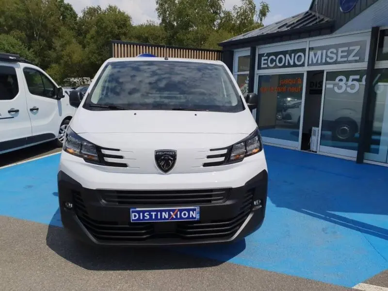 Vue avant d’un Peugeot Expert Fourgon blanc avec calandre noire et logo lion distinctif, stationné devant un bâtiment commercial.