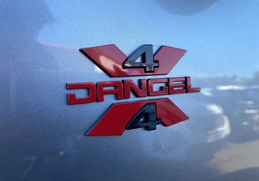 Gros plan sur l'écusson rouge Dangel 4x4 sur la carrosserie gris Artense métallisée du Peugeot Partner Fourgon 2025.