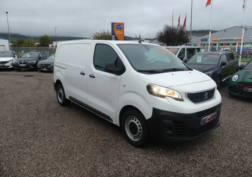 Fourgon Peugeot Expert blanc vu en 3/4 avant droit avec phares allumés sur parking extérieur.