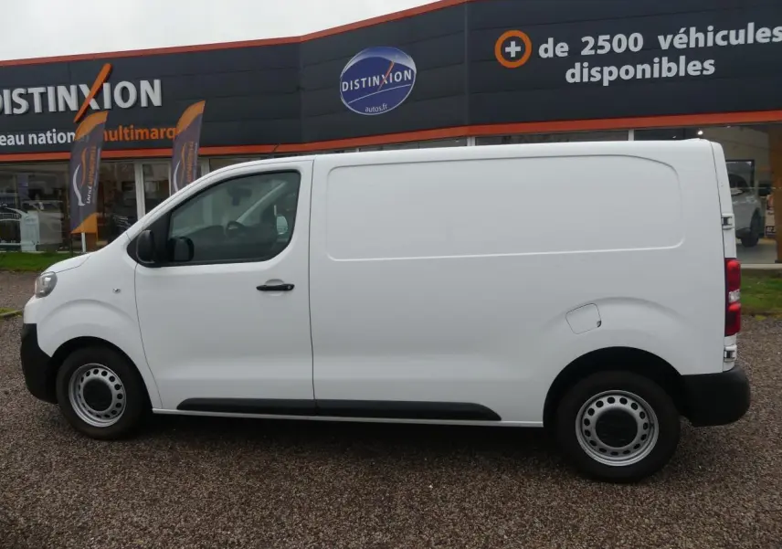 Vue de profil côté gauche d'un Peugeot Expert Fourgon blanc avec roues tôle et boucliers noirs sur parking.