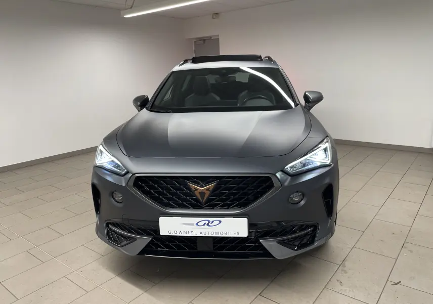 Vue avant d'un CUPRA Formentor 1.5 TSI 150 DSG7 VZ-LINE gris magnétique mat avec phares allumés en intérieur.