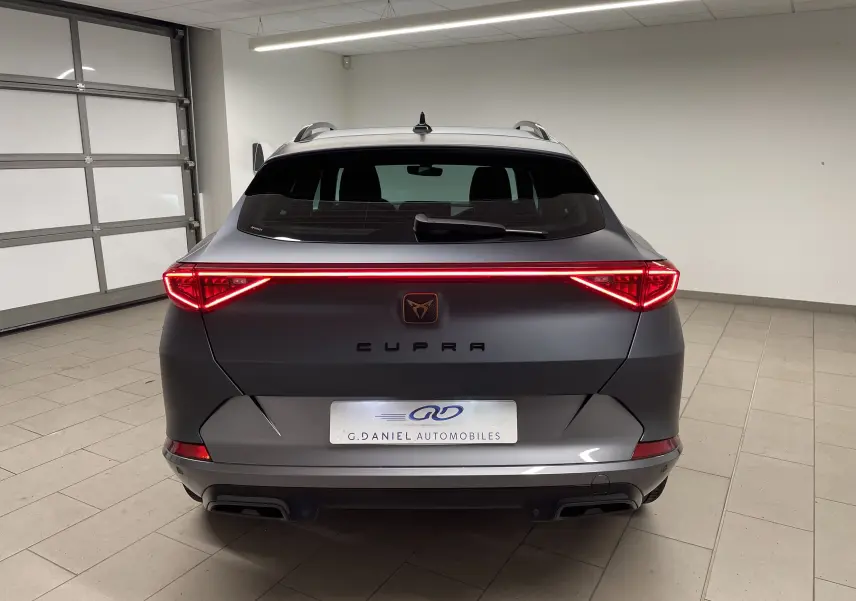 Vue arrière d'un CUPRA Formentor 1.5 TSI 150 DSG7 en gris magnétique mat avec feux LED allumés dans un garage.