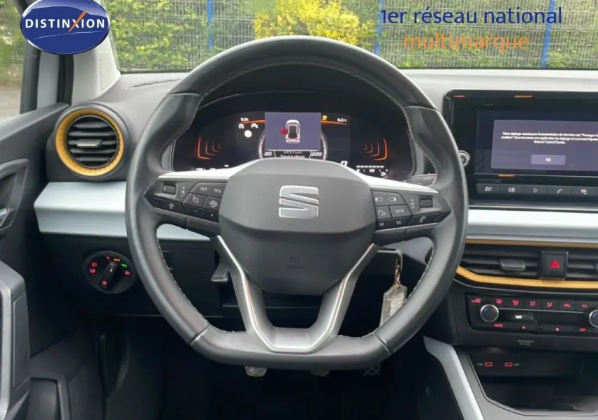 Vue intérieure centrée sur le volant noir de la SEAT Arona 2025, avec tableau de bord digital et détails jaunes autour des aérateurs.