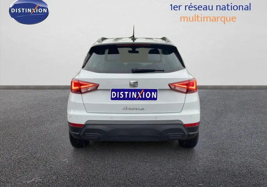 Vue arrière d'un SEAT Arona blanc alpin avec toit noir, feux arrière allumés, sur fond neutre intérieur.