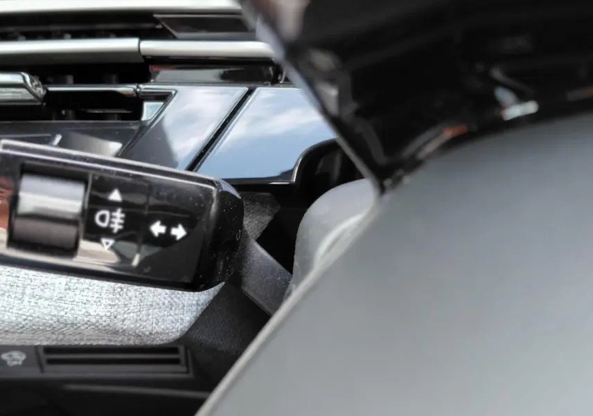 Gros plan sur la commande des feux avec réglage automatique dans l’habitacle du Peugeot 3008 Hybrid noir 2025.