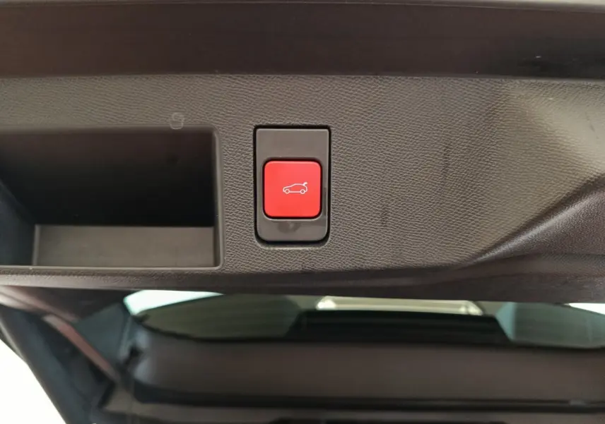 Bouton rouge d'ouverture électrique du coffre sur la partie intérieure du hayon d'une Citroën C5 noire hybride.