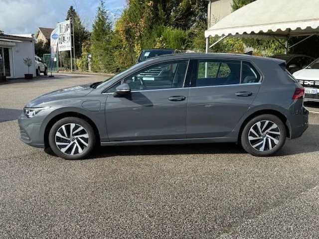Volkswagen Golf VIII 1.4 e-Hybrid gris dauphin vue 3/4 avant droit sur parking sous un ciel partiellement nuageux