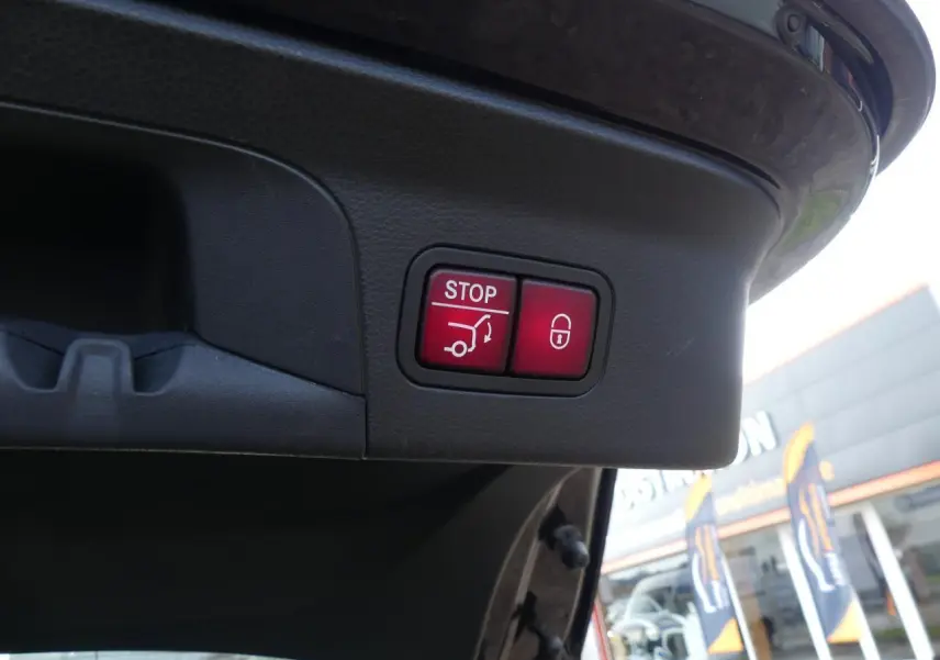 Gros plan sur les boutons rouges de fermeture et verrouillage électrique du hayon d’un Mercedes GLC Coupé bleu foncé.