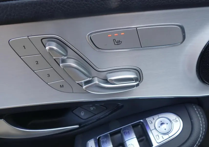 Gros plan sur les commandes de réglage de siège en aluminium brossé et cuir noir côté gauche d'une Mercedes GLC Coupé bleu foncé.