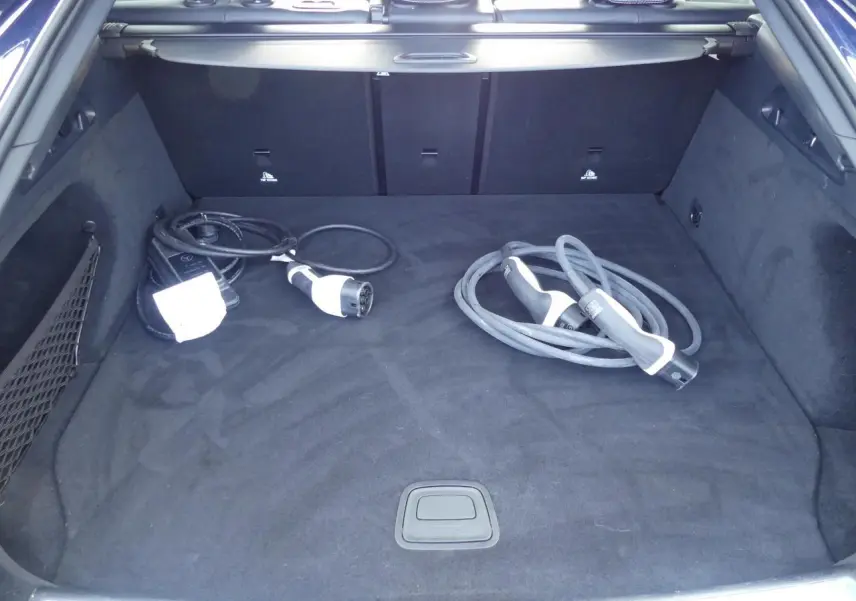 Coffre ouvert d’un Mercedes GLC Coupé hybride bleu foncé avec câbles de recharge sur tapis noir.