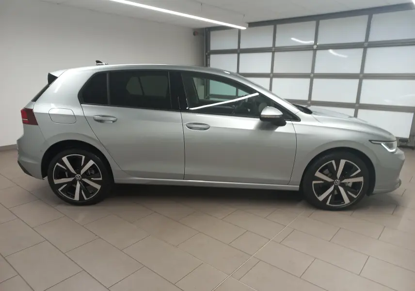 Vue de profil côté gauche d'une Volkswagen Golf 1.5 eHybrid 204 DSG6 argent Dolomite avec jantes alliage 18 pouces 'Catania' en intérieur.