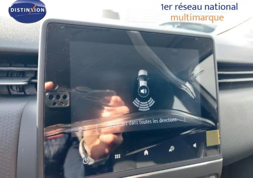 Écran tactile central du tableau de bord d’une Renault Clio blanche, affichant l’aide au stationnement.