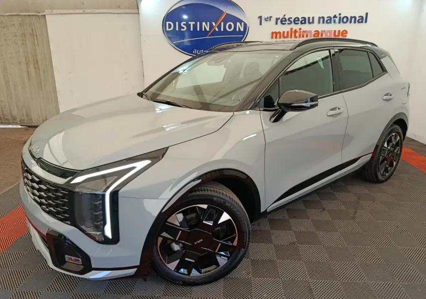 KIA Sportage gris clair en 3/4 avant droit, avec feux LED verticaux distinctifs et jantes noires stylées.