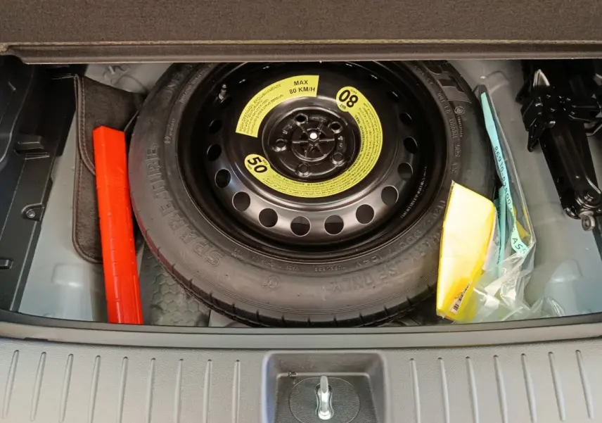 Vue plongeante sur la roue de secours noire dans le coffre du KIA SPORTAGE gris clair 2026, avec kit de sécurité adjacent.