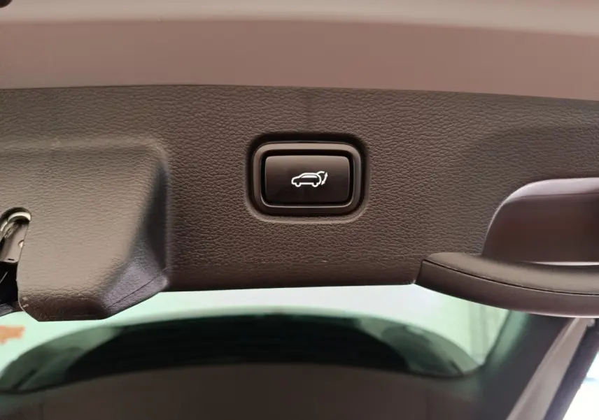 Gros plan sur le bouton d'ouverture électrique du coffre, intégré dans le hayon intérieur noir du KIA Sportage gris clair.