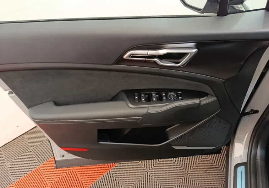 Vue intérieure de la porte avant gauche du Kia Sportage gris clair, avec commandes électriques et garniture noire.