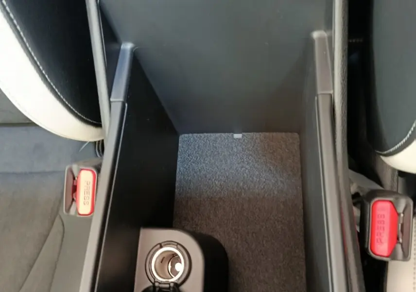 Vue plongeante sur la console centrale ouverte du Kia Sportage gris clair, montrant une prise 12V et les sièges clairs adjacents.