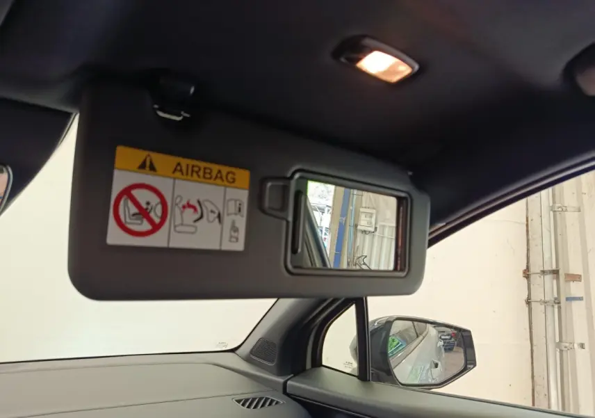 Détail de la visière côté conducteur avec miroir intégré et avertissement airbag, intérieur noir du Kia Sportage gris clair.