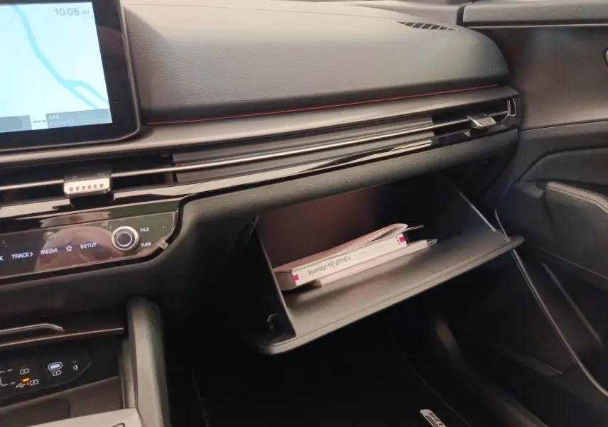 Intérieur du Kia Sportage 2026, vue côté passager sur la boîte à gants ouverte avec manuel visible, tableau de bord noir.