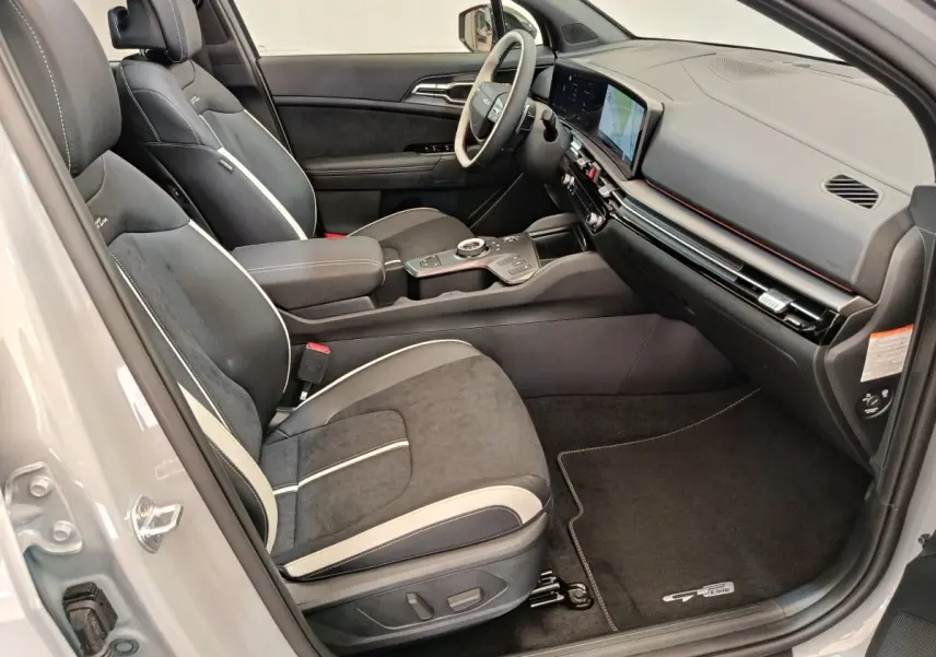 Vue intérieure côté passager du Kia Sportage gris clair 2026, sièges noirs avec surpiqûres blanches et tableau de bord moderne.
