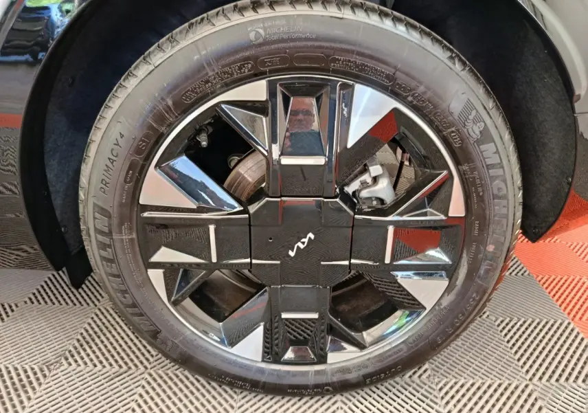 Gros plan sur la roue avant droite du Kia Sportage gris clair avec jante alliage noire et argentée au design géométrique.