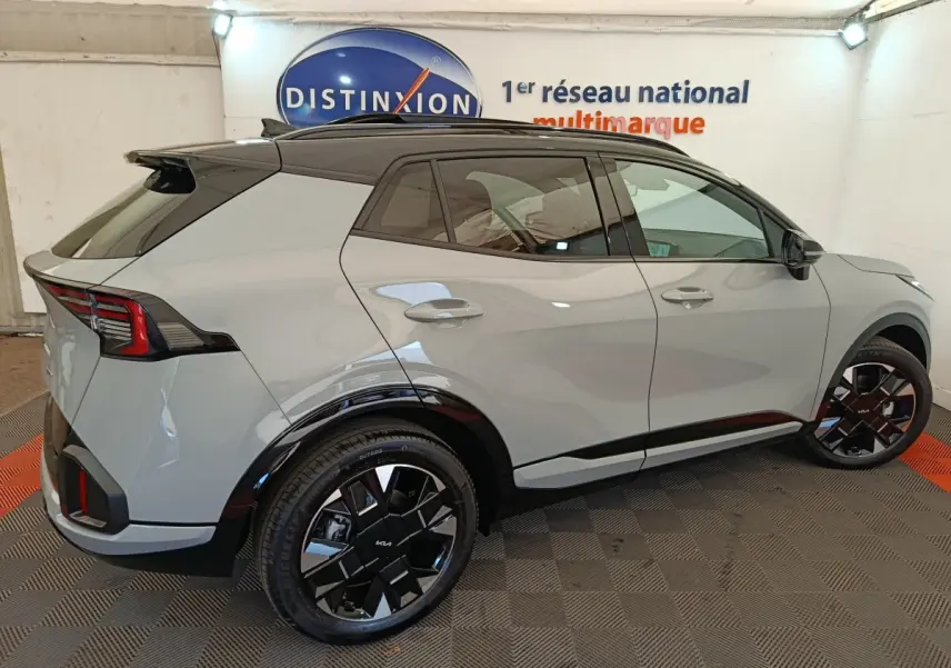 Vue 3/4 arrière droite du KIA SPORTAGE gris clair 2026 avec toit noir et jantes noires distinctives.